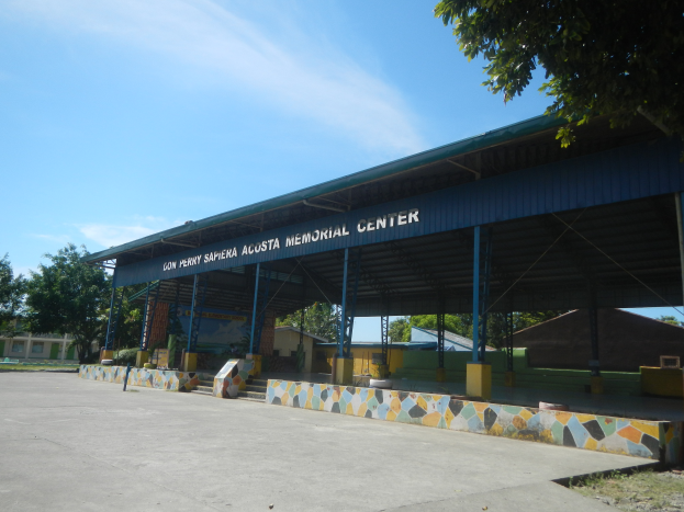 Der Eingang zu einem Gebäude mit einem Schild, das "Gedenkzentrum" lautet, umgeben von Bäumen, Häusern und einer Straße, mit einem Himmel voller weißer, flauschiger Wolken im Hintergrund.