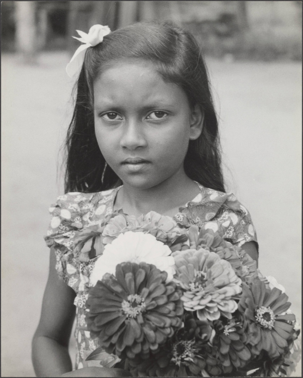 Ein junges Mädchen in Schwarz-Weiß hält einen Blumenstrauß und lächelt.
