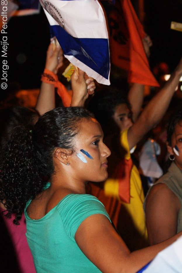 Frauen in grünen T-Shirts, die auf einer Demonstration stehen und weiße Schilder halten, mit vielen anderen Mädchen im Hintergrund.