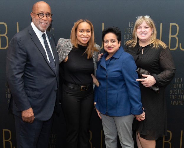 Eine Gruppe von vier Menschen, die auf einem roten Teppich stehen, lächeln und für ein Foto posieren, mit einem "Liberty Justice for All Awards"-Schild im Hintergrund.