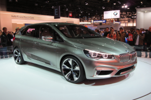 BMW 2er Active Tourer Concept auf der IAA in Frankfurt zu sehen, umgeben von Menschen, die es fotografieren, unter Deckenlampen mit Informationsschildern im Hintergrund.