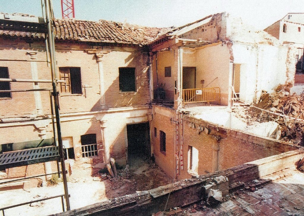 Teilweise abgerissenes Gebäude mit notdürftiger Barriere, sichtbaren Fenstern und einer leiterähnlichen Struktur.