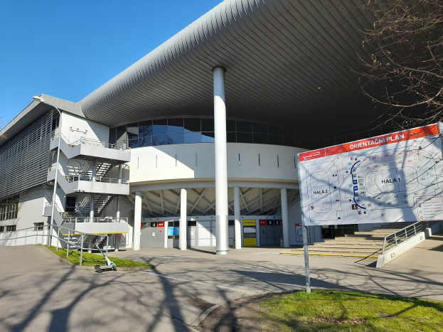 Ein großes Gebäude mit vielen Fenstern, Säulen und Treppen, das als Eingang zum Olympiastadion in London dient, mit einem Wagen, Gras, einer Straße, Bäumen und einem Himmel im Hintergrund.