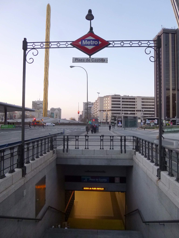 Eine belebte Stadtkulisse mit Gebäuden, Fahrzeugen, Fußgängern, einem U-Bahn-Eingang und einem Bogen mit einer Tafel im Hintergrund.