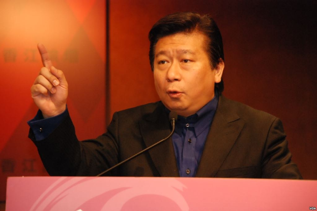 Ein Mann in Anzug und Krawatte, der hinter einem Rednerpult spricht und ernst dreinschaut.