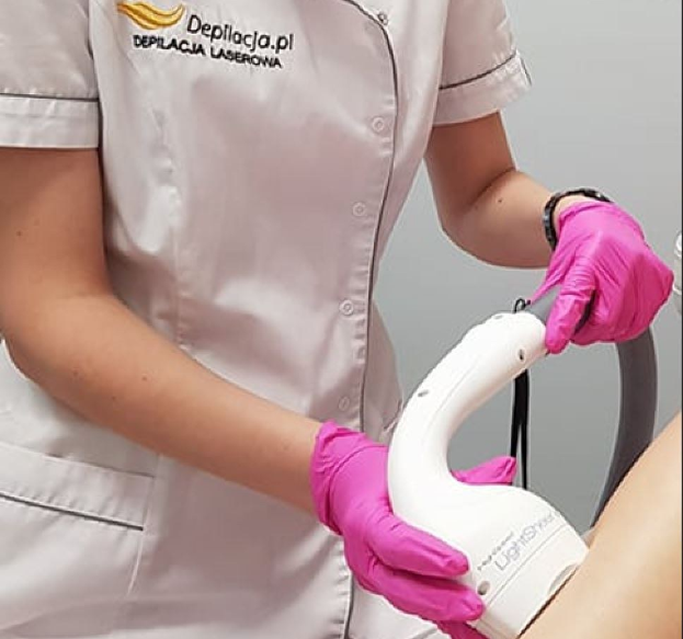Eine Frau in einem weißen Hemd und pinken Handschuhen bedient eine weiße Laser-Haarentfernungsmaschine auf ihrer Haut und steht vor einer Wand.