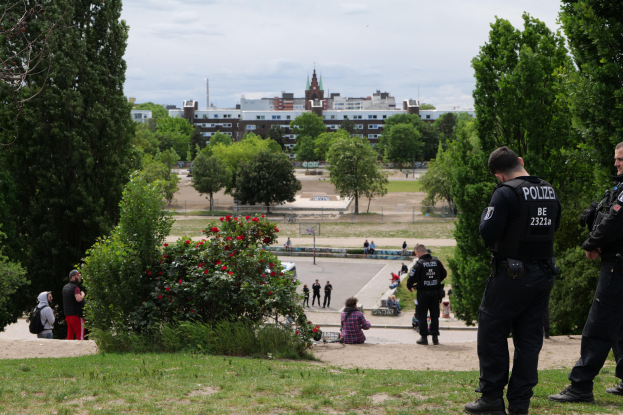 Zwei Polizeibeamte vor einer Gruppe von Menschen in einem Park mit saftig grünem Gras, Bäumen, bunten Blumen, Gebäuden, Polen und einem klaren blauen Himmel.