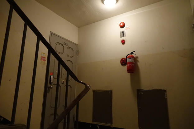 Treppenhaus mit einem an der rechten Wand montierten Feuerlöscher, einem Geländer auf der linken Seite, zwei Türen im Hintergrund und einer Lampe oben.