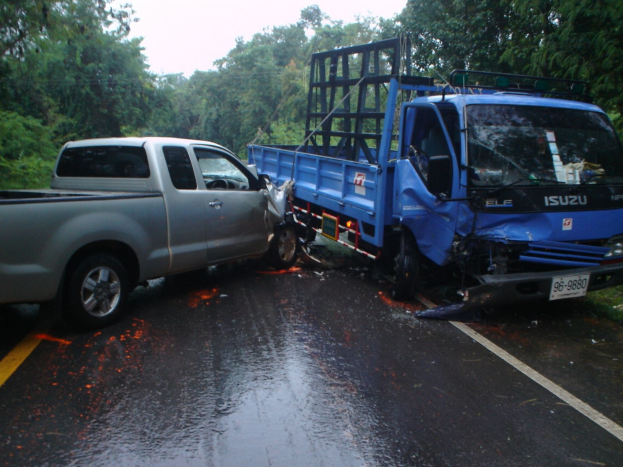 Ein schwerbeschädigter Lkw mit eingedrückter Front und verbeulter Karosserie liegt auf der Seite einer Straße, umgeben von Bäumen unter einem klaren blauen Himmel.
