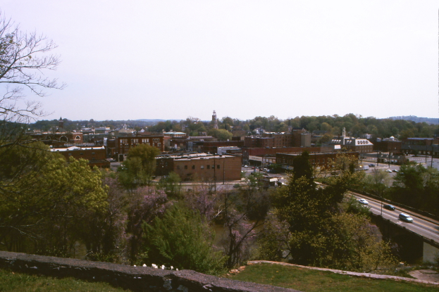 Eine Stadtansicht mit Gebäuden, Bäumen, Polen, Straßen, Fahrzeugen und einem Himmel.