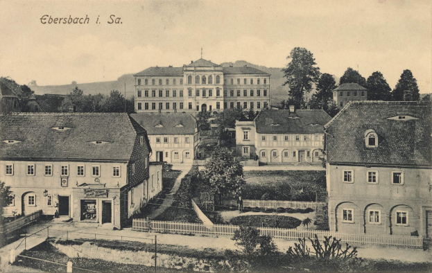 Ein altes Schwarz-Weiß-Foto von Ebersbach, Deutschland, circa 1900, das Gebäude, Bäume, Pflanzen, Gras, einen Zaun und einen Himmel im Hintergrund zeigt.