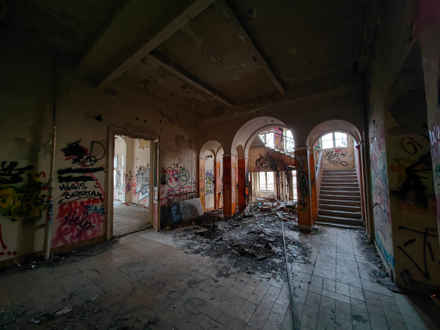 Ein verlassener Gebäudeinnenraum mit Graffiti an den Wänden und Treppen, Schutt auf dem Boden und verstreuten Gegenständen.