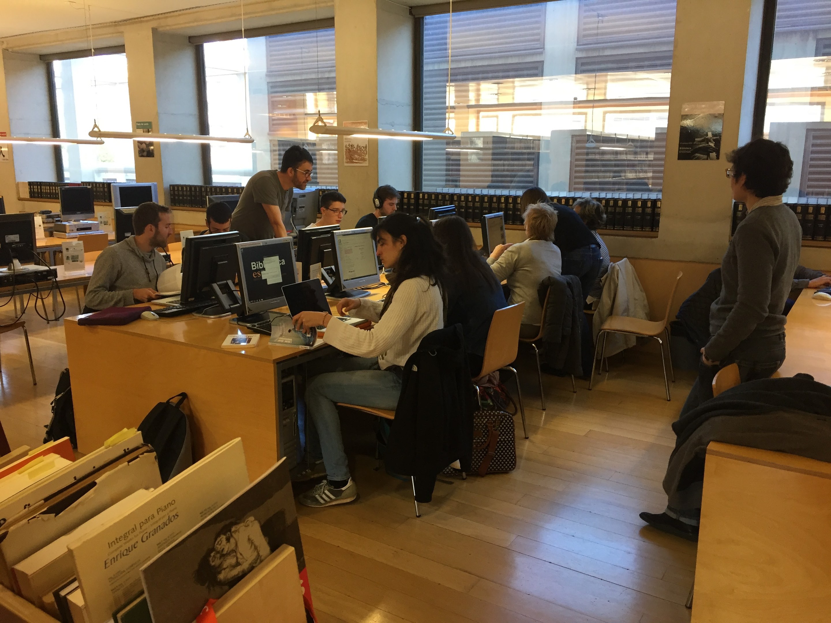 Eine Gruppe von Menschen, die an Computern auf Schreibtischen in einer Bibliothek arbeiten.