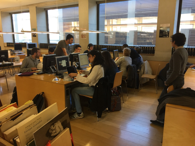 Eine Gruppe von Menschen, die an Computern auf Schreibtischen in einer Bibliothek arbeiten.