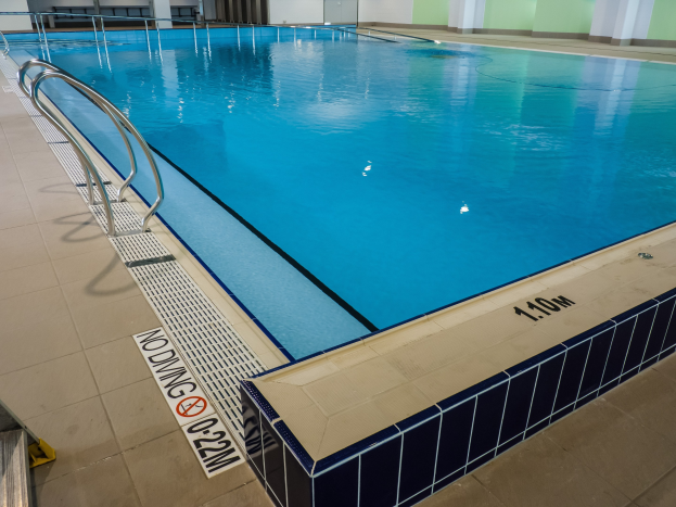 Indoor-Schwimmbad mit gefliestem Boden, Metallstützen, einem Schild, einer Tür und Deckenlampen in einem großen Gebäude.