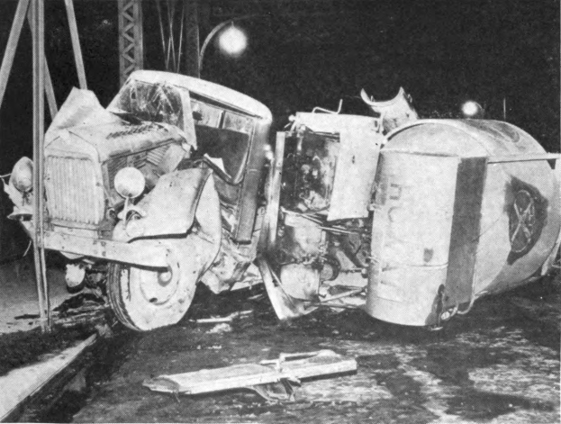Ein Schwarz-Weiß-Foto eines umgestürzten Autos aus den 1930er Jahren auf der Straße, mit Metallstangen und einem Laternenpfahl im Hintergrund.