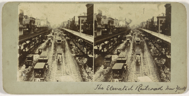 Schwarzes und weißes Foto eines Zuges auf einer Hochbahn in New York City mit mehreren Fahrzeugen auf den Schienen, Menschen und Gebäuden im Hintergrund, einschließlich Text am unteren Rand.