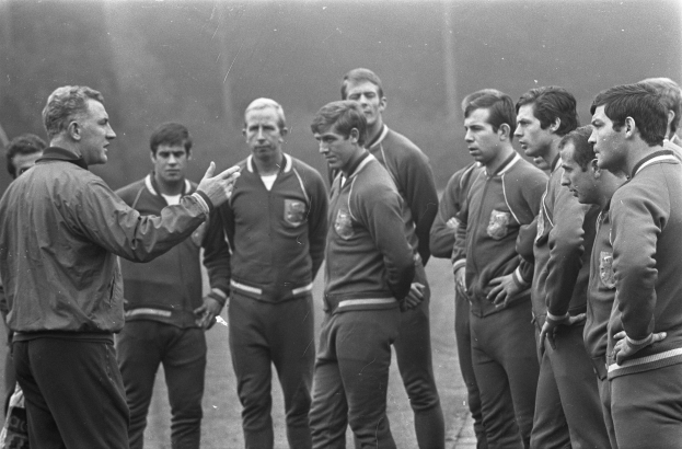 Ein Schwarz-Weiß-Foto einer Gruppe von Männern auf einem Fußballfeld, wobei der Mann in der Mitte einen Walking-Schuh trägt.