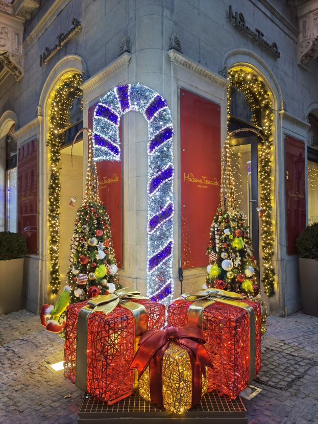 Ein festlich geschmücktes Gebäude mit zwei beleuchteten Weihnachtsbäumen und Geschenkboxen auf dem Boden sowie Topfpflanzen.