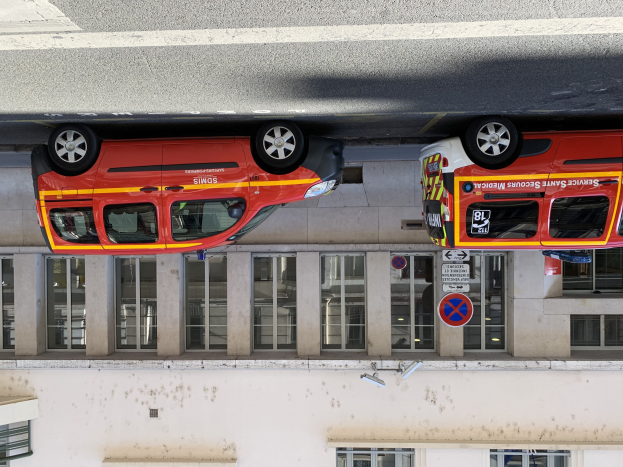 Zwei Rettungswagen nebeneinander in einer Tiefgarage geparkt, mit einem Gebäude mit Glasfenstern und Schildern im Hintergrund und einer Überwachungskamera an der Wand unten.