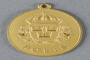 Eine goldene Medaille mit einer kronenförmigen Polizeimarke mit eingravierter Schrift in der Mitte.