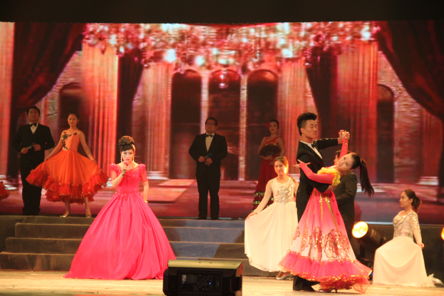 Eine Gruppe von Menschen auf einer Bühne mit Scheinwerfern, Stufen und einem Hintergrundbild, mit einem Lautsprecher unten, der eine Tanzvorstellung suggeriert.