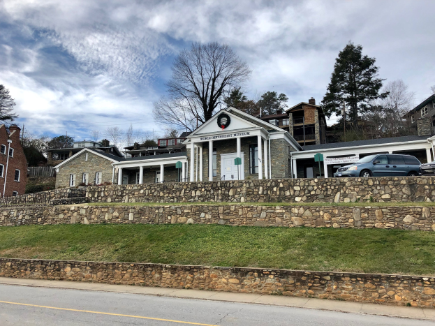 Steinwand mit geparkten Autos, angrenzende Gebäude mit Fenstern und Türen, Bäume und ein bewölkter Himmel im Hintergrund, als das kürzlich wiedereröffnete Weltkulturerbe-Museum bezeichnet.