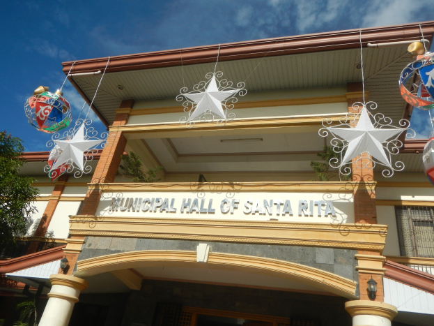Municipal Hall of Santa Rita mit Fenstern, Säulen, einem Namensschild, dekorativen Dachschmuck, einem Baum links und einem bewölkten Himmel als Hintergrund.