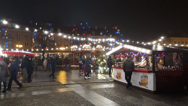 Ein nächtlicher Weihnachtsmarkt in einer Stadt mit Menschen, beleuchteten Ständen, geschmückten Gebäuden und festlicher Beleuchtung am Himmel.