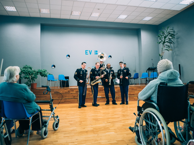 Eine Gruppe von Menschen im Rollstuhl, die in einem Raum mit Stühlen, Pflanzen und Deckenleuchten Musikinstrumente spielen, mit einigen Individuen, die auf Stühlen sitzen, was auf ein Rollstuhlband-Event hindeutet.