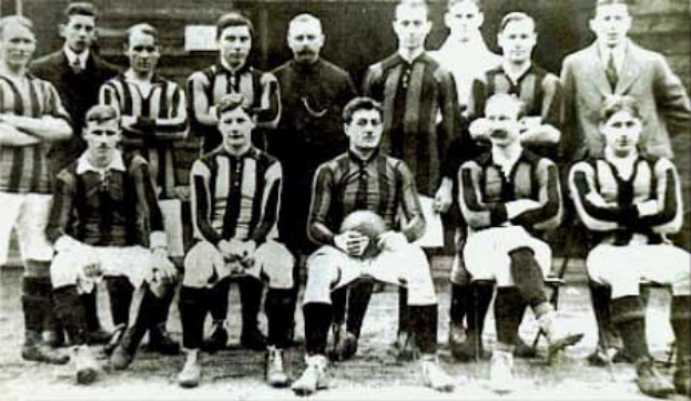 Ein Schwarz-Weiß-Foto einer Fußballmannschaft, wobei einige stehen und einige sitzen, vor einer Wand, mit dem Text "Ballymena Football Club" unten.