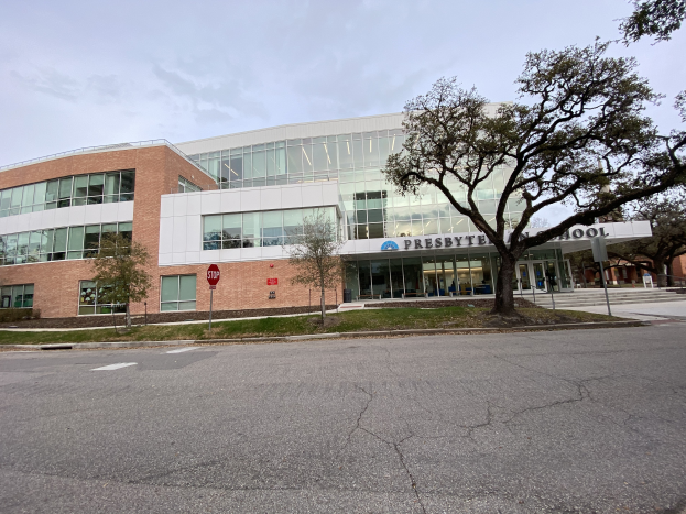 Presbyte Mittelschule, ein großes Gebäude mit vielen Fenstern, umgeben von Bäumen, Gras, Schildern, Pfählen und einer Straße, mit bewölktem Himmel im Hintergrund.