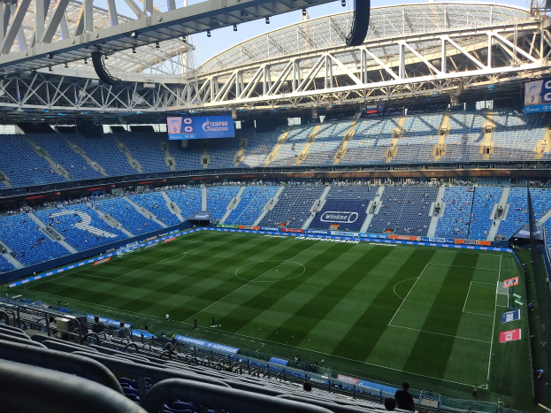 Ein großes Stadion mit einem Fußballfeld in der Mitte, umgeben von Stühlen, Geländern, Tafeln mit Text, Lampen und anderen Gegenständen, identifiziert als Estadio Santiago Bernabeu, Heimstadion von Real Sociedad, mit dem Himmel im Hintergrund.