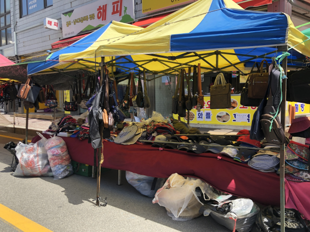 Ein Markt mit Zelten, die Taschen, Hüte und andere Gegenstände präsentieren, vor Häusern mit Fenstern und Schildern.