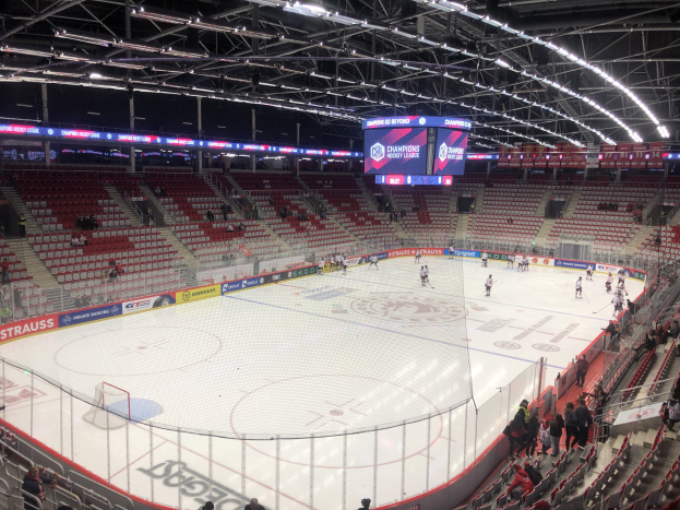 Eishockeyspiel in einer großen Arena zwischen den St. Louis Blues und Detroit Red Wings, mit Zuschauern auf Sitzen und Stehplätzen in der Nähe der Eisfläche umgeben von einem Zaun und einem Anzeigebildschirm.