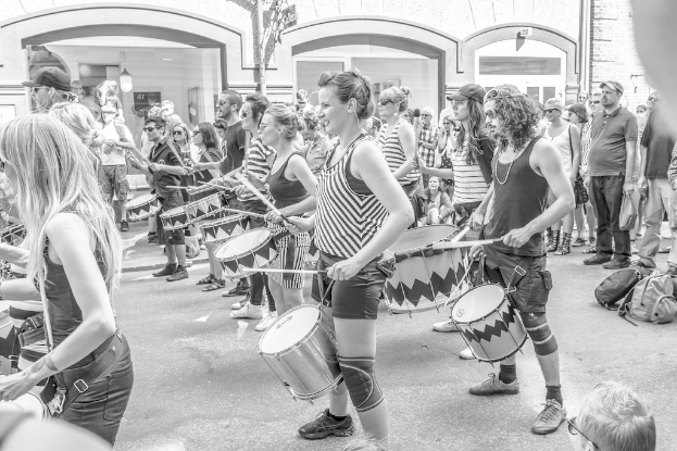Eine Gruppe von Menschen, die draußen vor einer geschlossenen Glastür mit einer Leuchte im Hintergrund Musikinstrumente spielen.