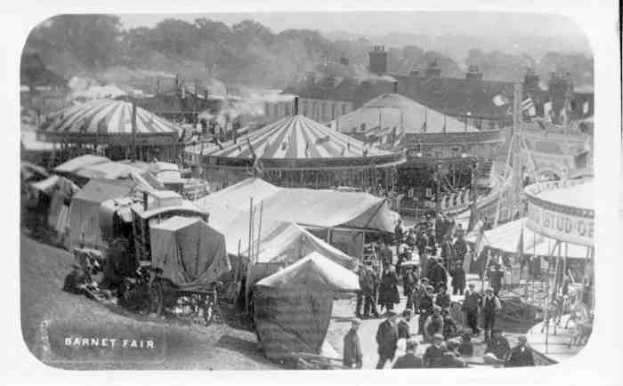 Ein altes Schwarz-Weiß-Foto einer lebhaften KarnevalsSzene mit Zelten, Menschen, Karren, Pfählen, Bäumen und Gebäuden im Hintergrund, beschriftet mit "Barnet Fair, London, England".