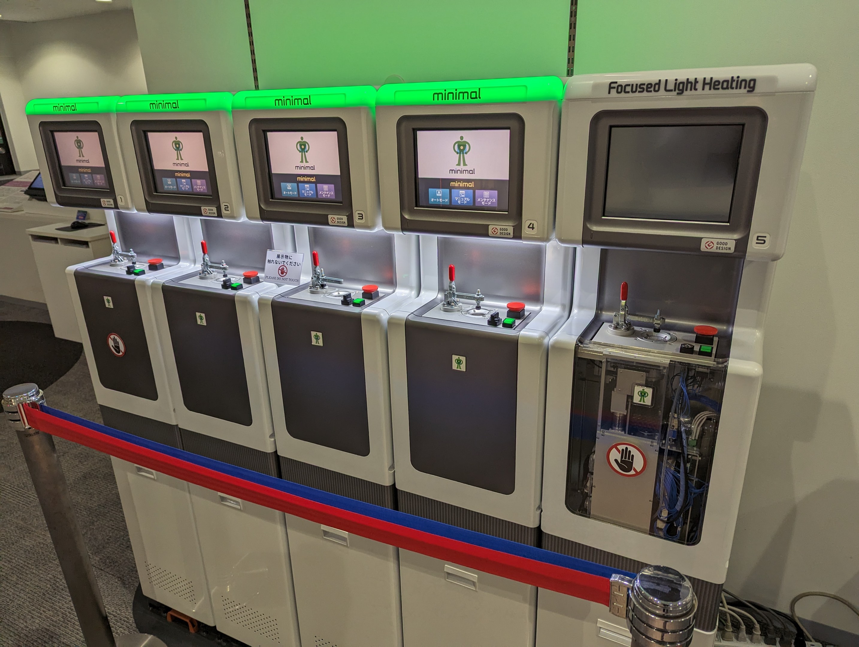 Eine Reihe von Mini-Heizungssystemgeräten mit Knöpfen und Drehreglern, die in einem Raum mit einer Wand, Deckenleuchten und einem Boden aufgereiht sind.