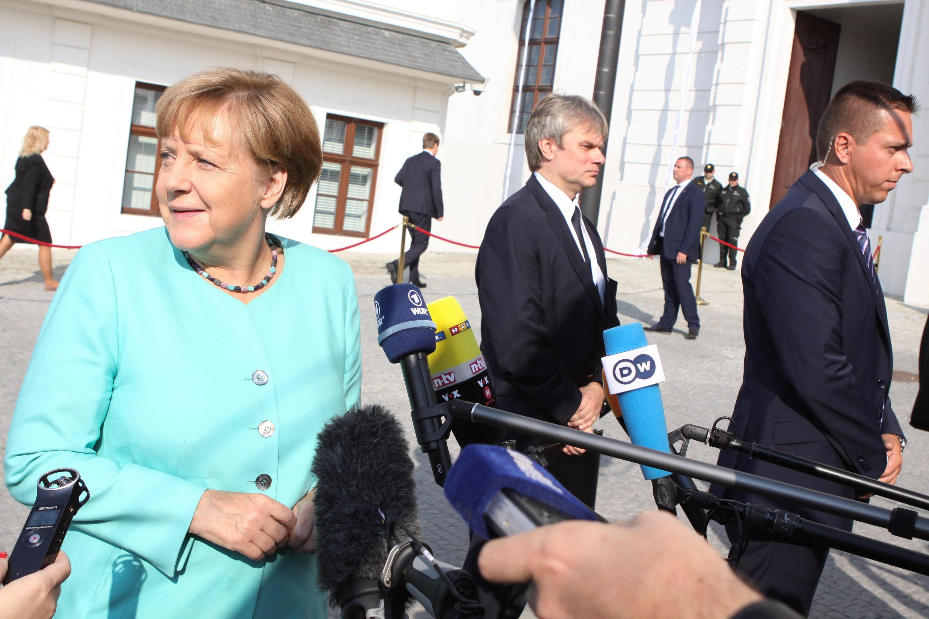 Bundeskanzlerin Angela Merkel spricht mit Reportern vor dem Kanzleramt in Berlin, umgeben von Menschen mit Mikrofonen und Gebäuden im Hintergrund.