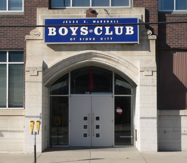 Das Boys Club Gebäude von Sioux City mit Glasfenstern und -türen, einer Tafel mit Text darauf und einem Pfosten auf dem Gehweg.