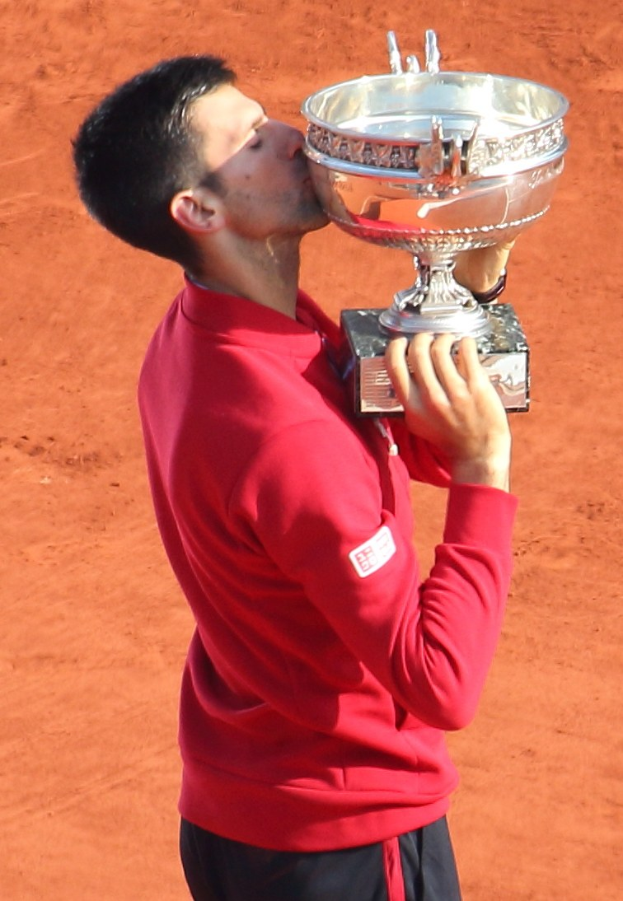 Novak Djokovic hält den French Open-Pokal und feiert nach dem Sieg gegen Rafael Nadal im Finale der Herren-Einzel, mit einem triumphierenden Gesichtsausdruck.