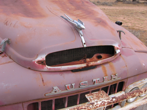 Alter rostiger Lastwagen auf einem Feld mit Bäumen und einem klaren blauen Himmel, von Rost bedeckt durch langanhaltende Witterungseinflüsse.