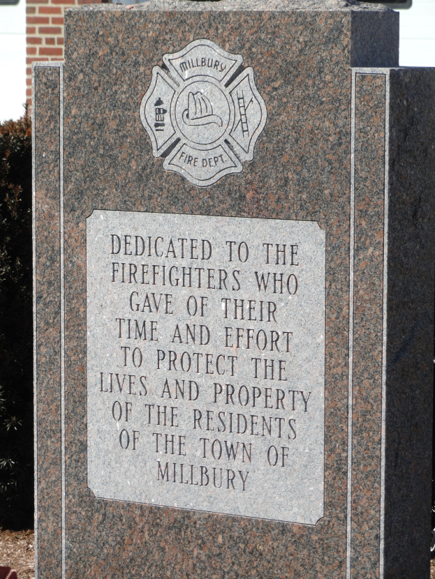 Gedenkstein mit einer Plakette für Feuerwehrleute, die die Inschrift trägt: 'Den Feuerwehrleuten, die ihre Zeit und Energie geopfert haben, um das Leben und Eigentum der Bewohner der Stadt Millbury zu schützen.'