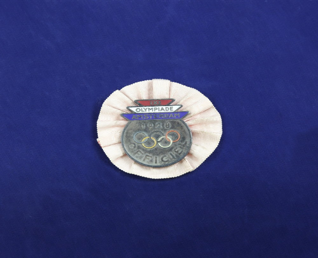 Blauer Stoff mit einem zentralen Olympischen Logo-Abzeichen, das wahrscheinlich eine Medaille anzeigt.