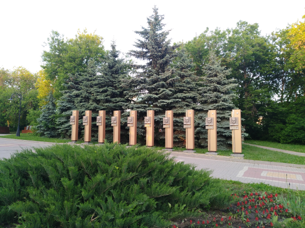 Ein Park mit einem Weg, Bäumen, Blumen, Gras und einem Straßenmast unter einem bewölkten Himmel, mit einer Gedenktafel für die Opfer der Tschernobyl-Katastrophe.