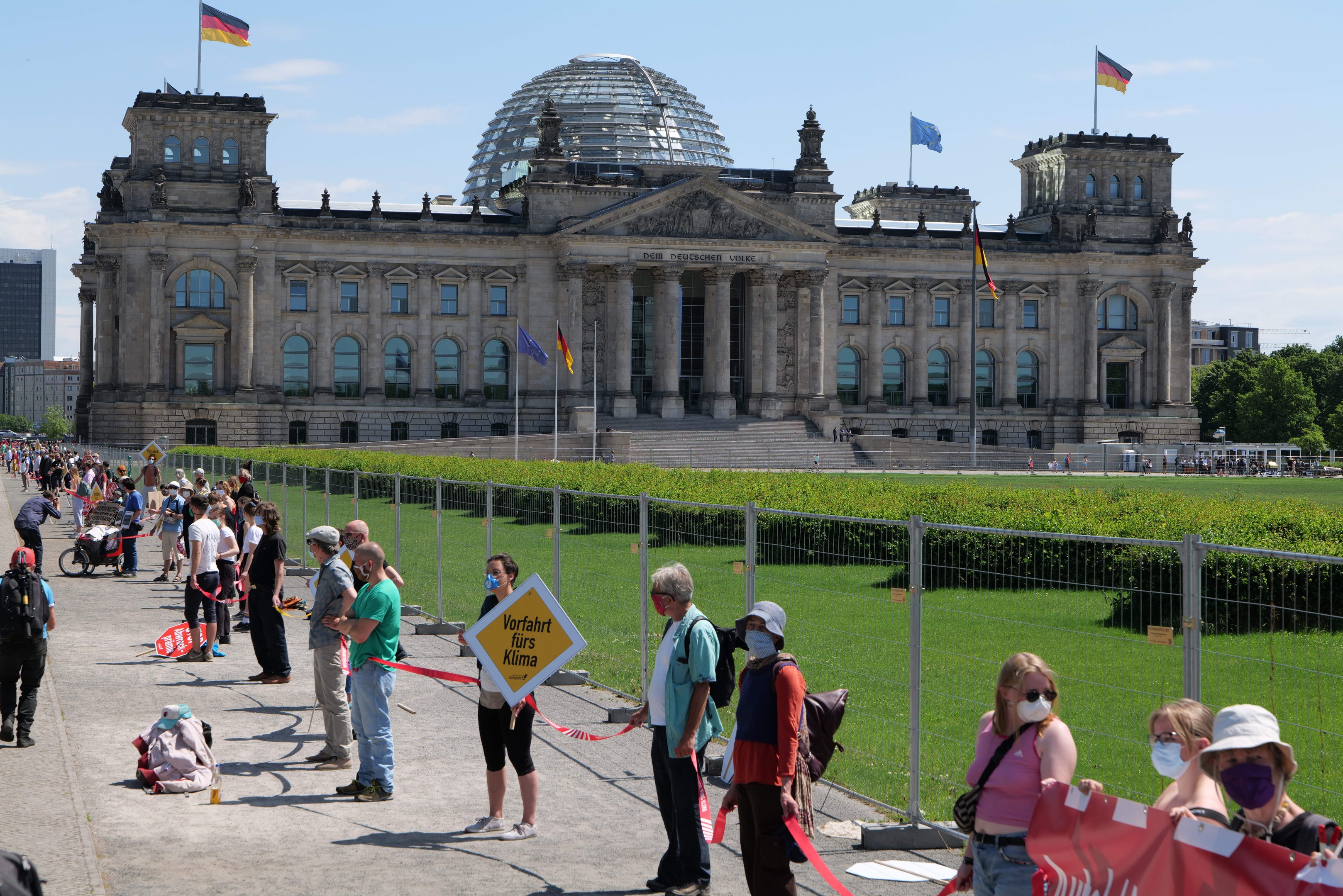 Gruppe von Menschen vor dem Reichstag in Berlin, einige tragen Mützen und Schutzbrillen, andere halten Schilder und einen Kinderwagen.