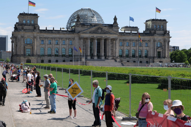Gruppe von Menschen vor dem Reichstag in Berlin, einige tragen Mützen und Schutzbrillen, andere halten Schilder und einen Kinderwagen.