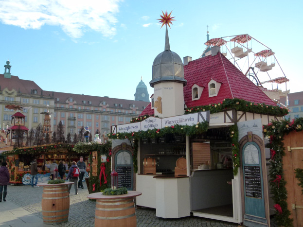 Ein belebter Weihnachtsmarkt in Nürnberg, Deutschland mit Menschen um geschmückte Stände, festliche Lichter, ein Riesenrad im Hintergrund und eine Schautafel rechts.
