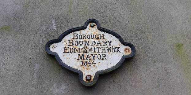 Metallplatte an einem Gebäude, die die Stadtteilgrenze markiert, mit "Edm Smithwick Bürgermeister" in fetter weißer Schrift auf einem schwarzen Hintergrund.