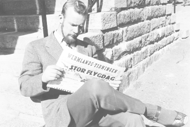 Ein Mann in einem Anzug sitzt auf einer Treppe und liest eine Zeitung mit ernster Miene in einem Schwarz-Weiß-Foto.